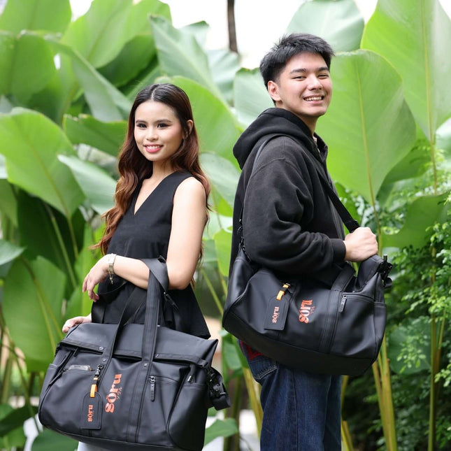 Young couple holding Kaze Duffel Bag & Weekender Bag Waterproof outdoors among green plants.