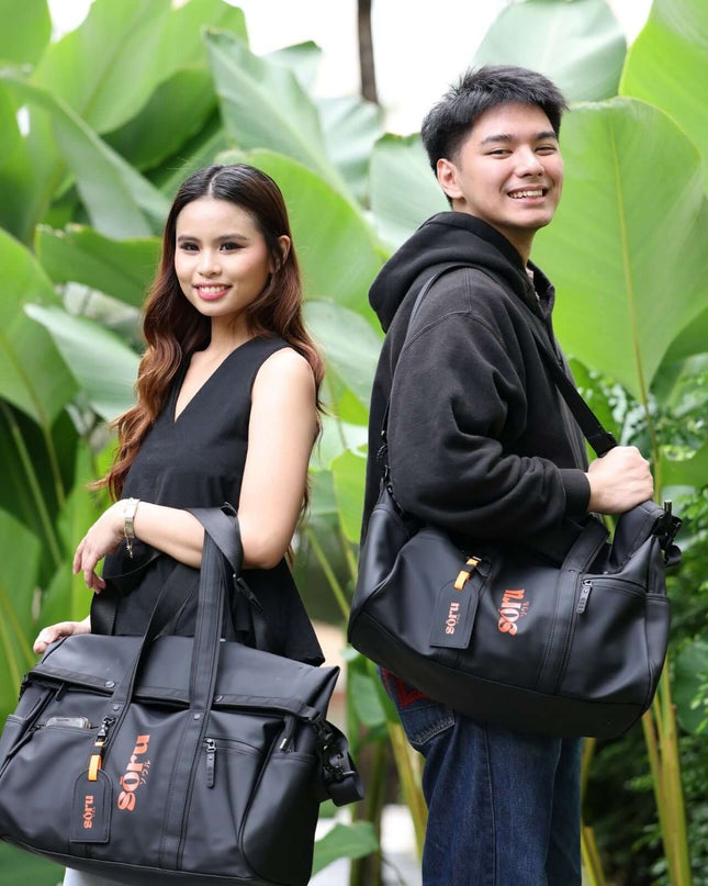 Young couple holding Kaze Duffel Bag & Weekender Bag Waterproof outdoors among green plants.