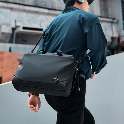 Person wearing a dark green jacket with a black bag over their shoulder, standing on a concrete surface.
