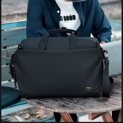 Black duffel bag on a wooden table with a person sitting in the background