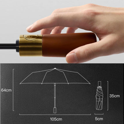 Hand holding the elegant wooden handle of the Amaya Tri-Fold Umbrella, showcasing its stylish design and brass button.